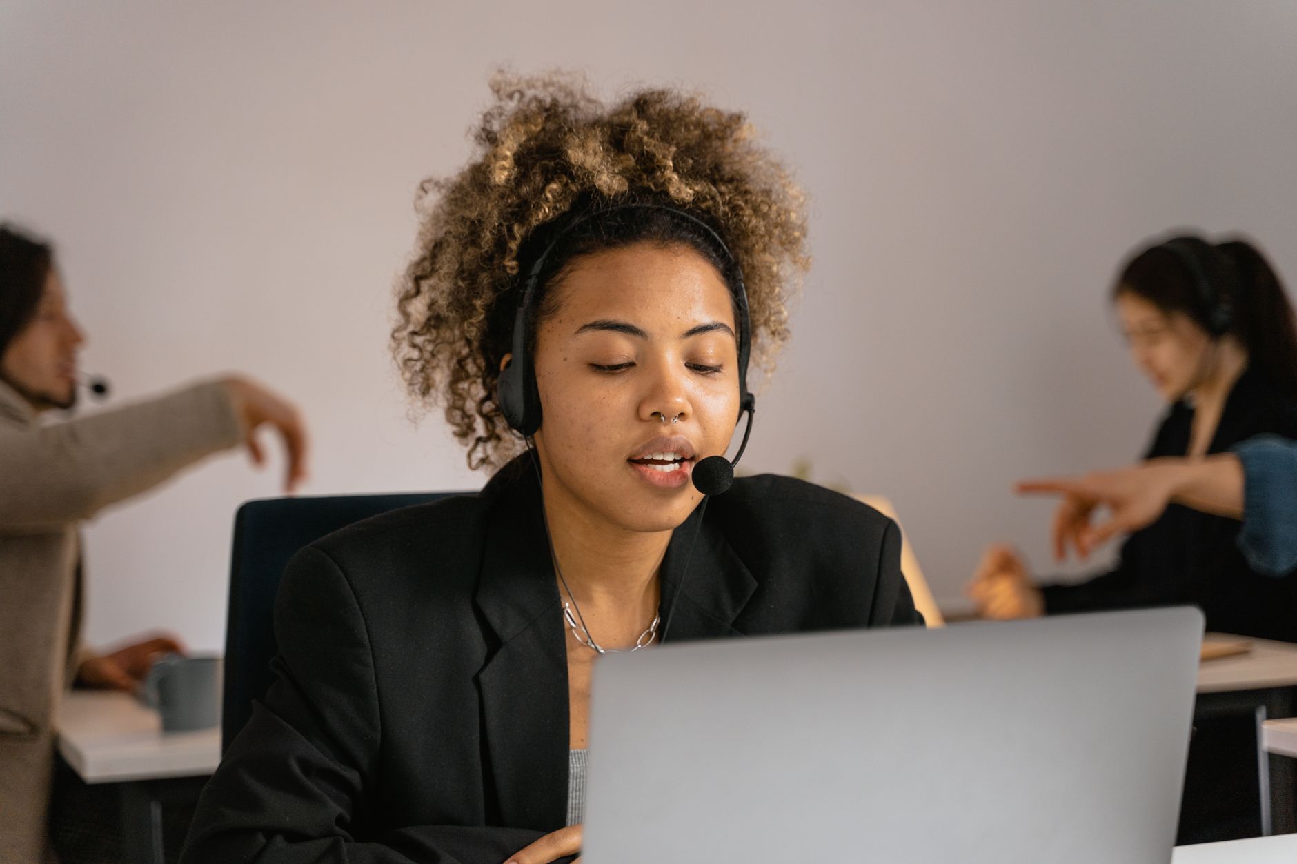 Persona con auriculares con micrófono trabajando ante un portátil en una oficina.