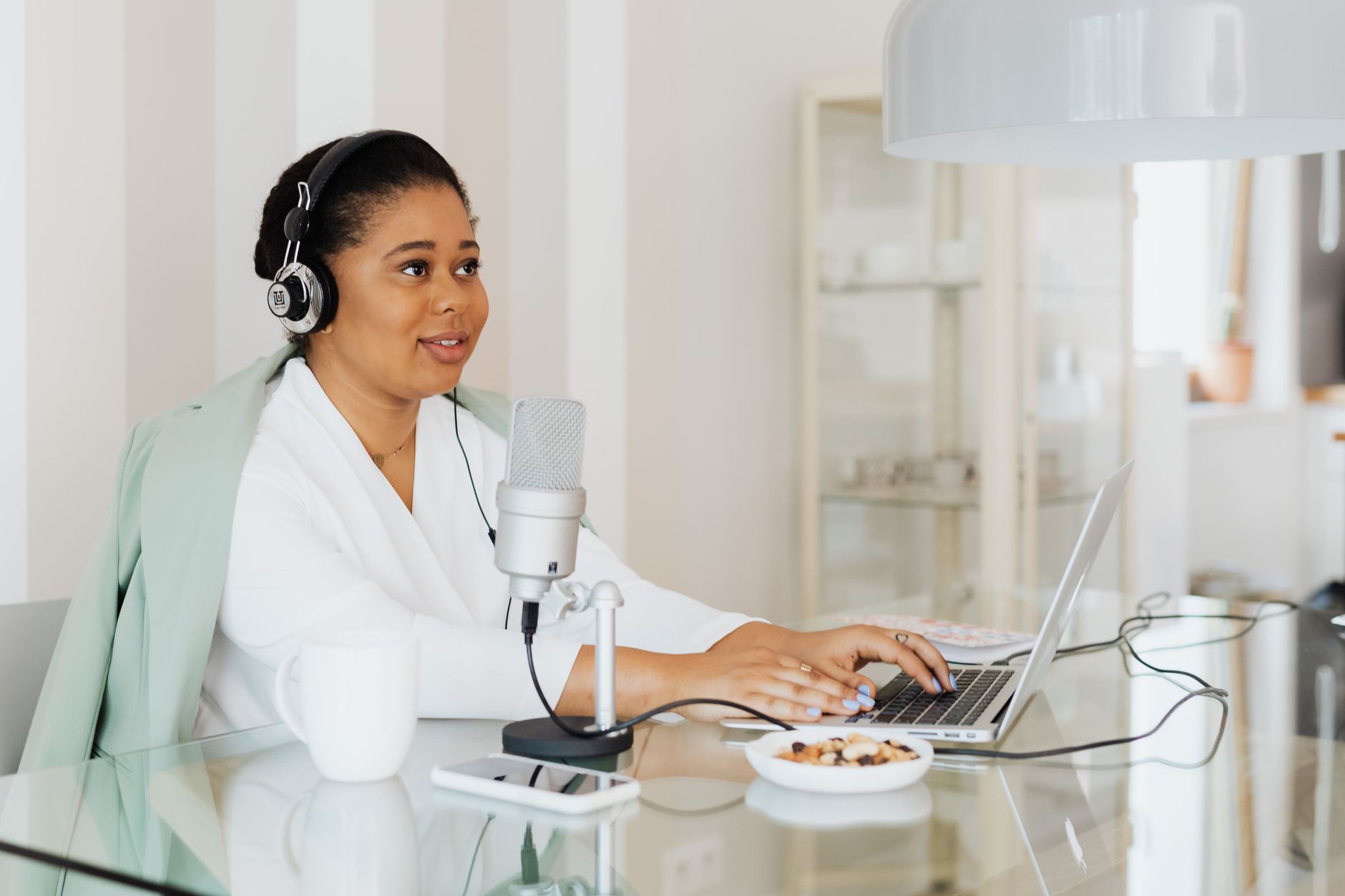 Mujer con auriculares hablando ante un micrófono mientras escribe en un portátil.